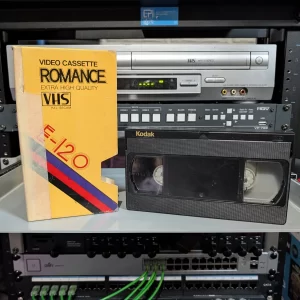 Black Kodak VHS beside a yellow Romance E-120 sleeve; neither shows a program title.