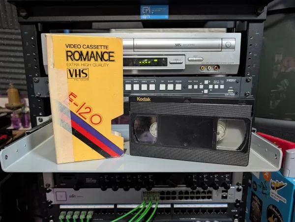 Black Kodak VHS beside a yellow Romance E-120 sleeve; neither shows a program title.