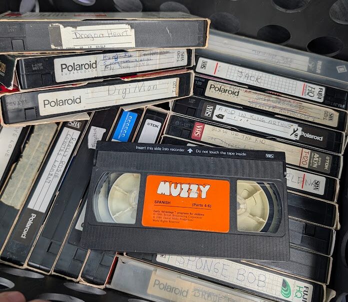 Handwritten and commercial VHS tapes piled inside a Goodwill bin