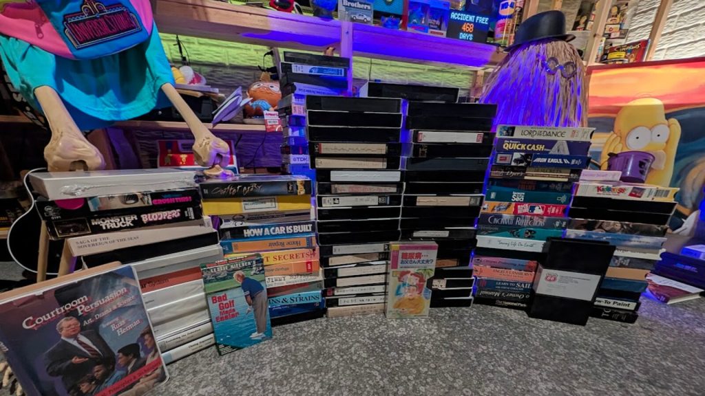 Where to find VHS tapes: piles of labeled VHS tapes and loose boxes in a cluttered archive room