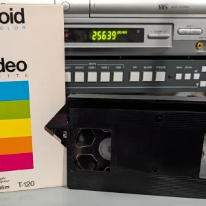 Black VHS cassette beside a white Polaroid Supercolor T-120 sleeve.