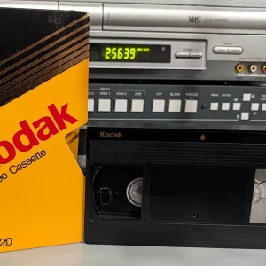 Yellow and black Kodak T-120 VHS sleeve beside a black Kodak tape on a shelf.