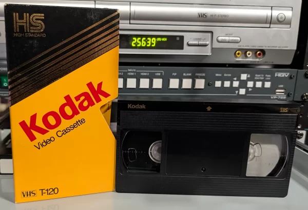 Yellow and black Kodak T-120 VHS sleeve beside a black Kodak tape on a shelf.