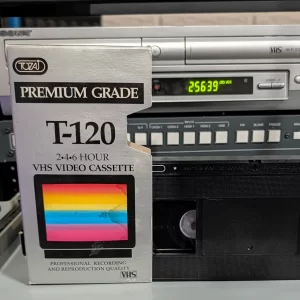TOZAI Premium Grade T-120 VHS sleeve in front of a partially visible black tape and video equipment.