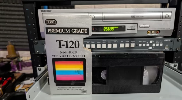 TOZAI Premium Grade T-120 VHS sleeve in front of a partially visible black tape and video equipment.