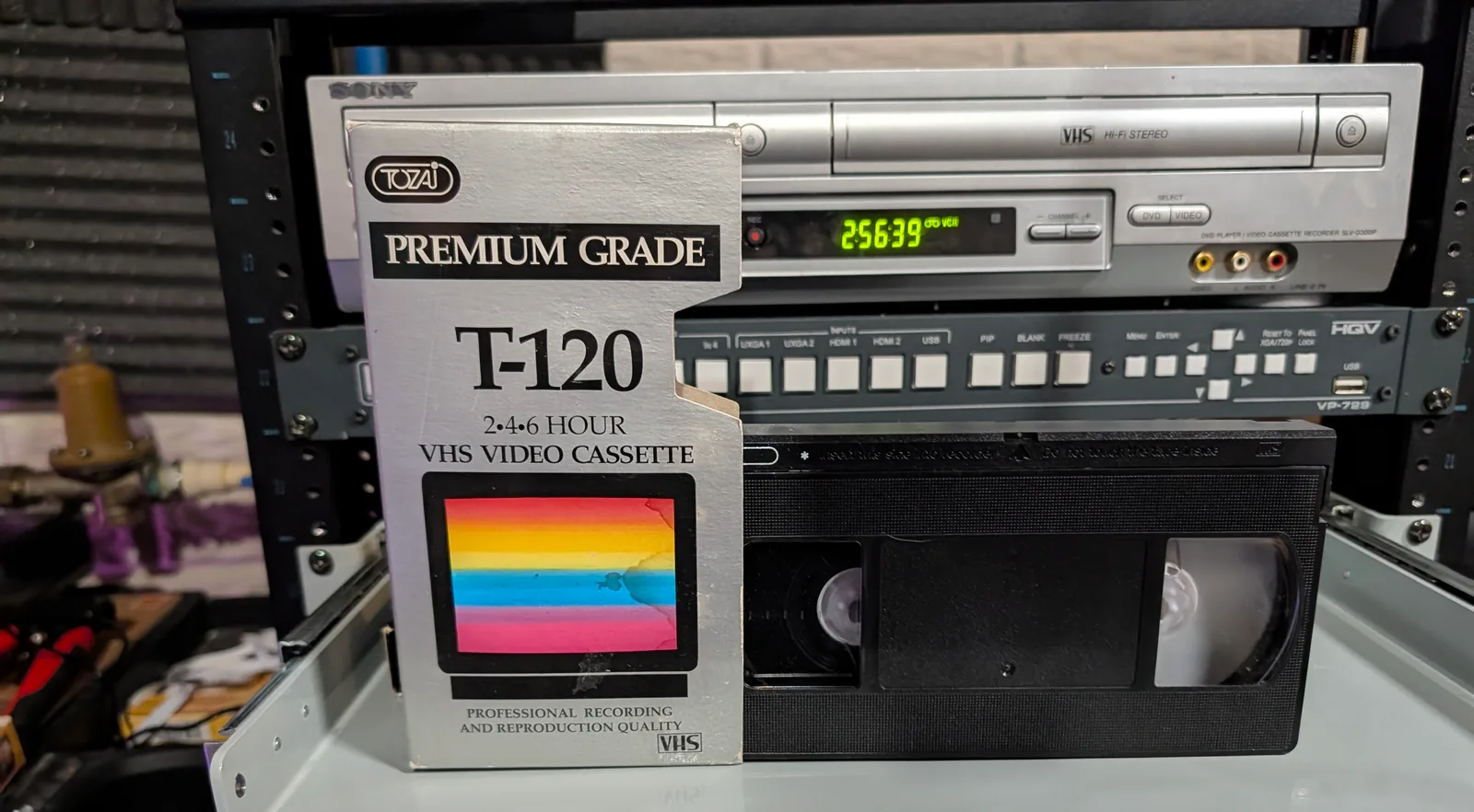TOZAI Premium Grade T-120 VHS sleeve in front of a partially visible black tape and video equipment.